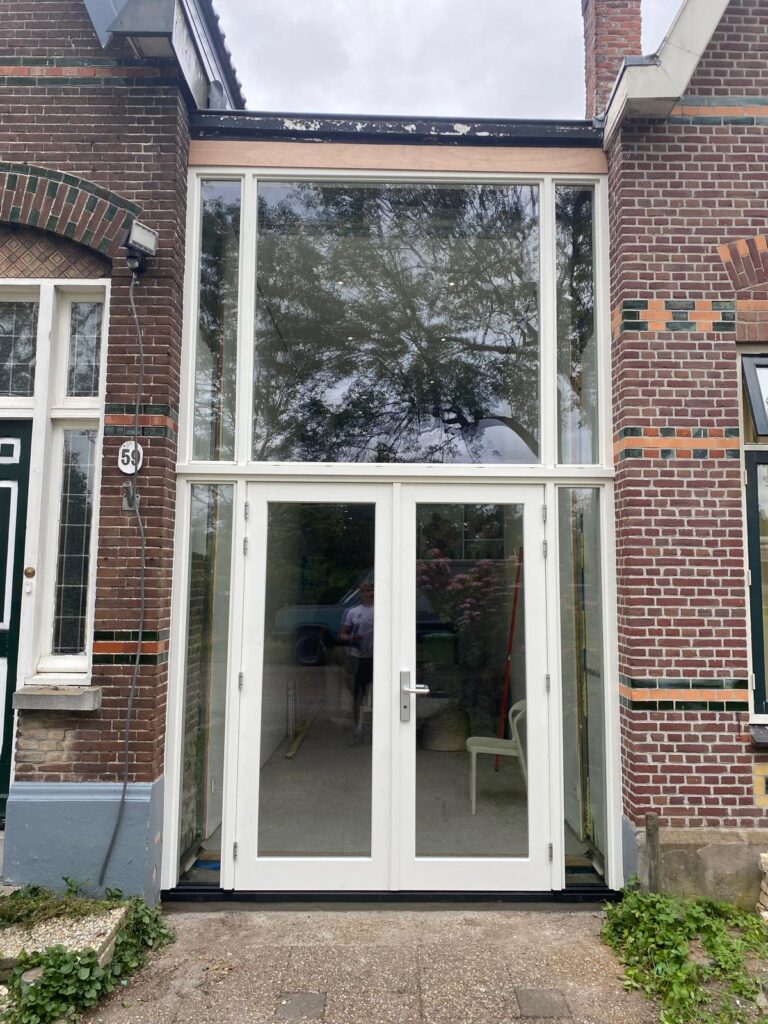 Vooraanzicht van de hoge hardhouten pui tussen de karakteristieke muren aan de Oude Kleiweg.