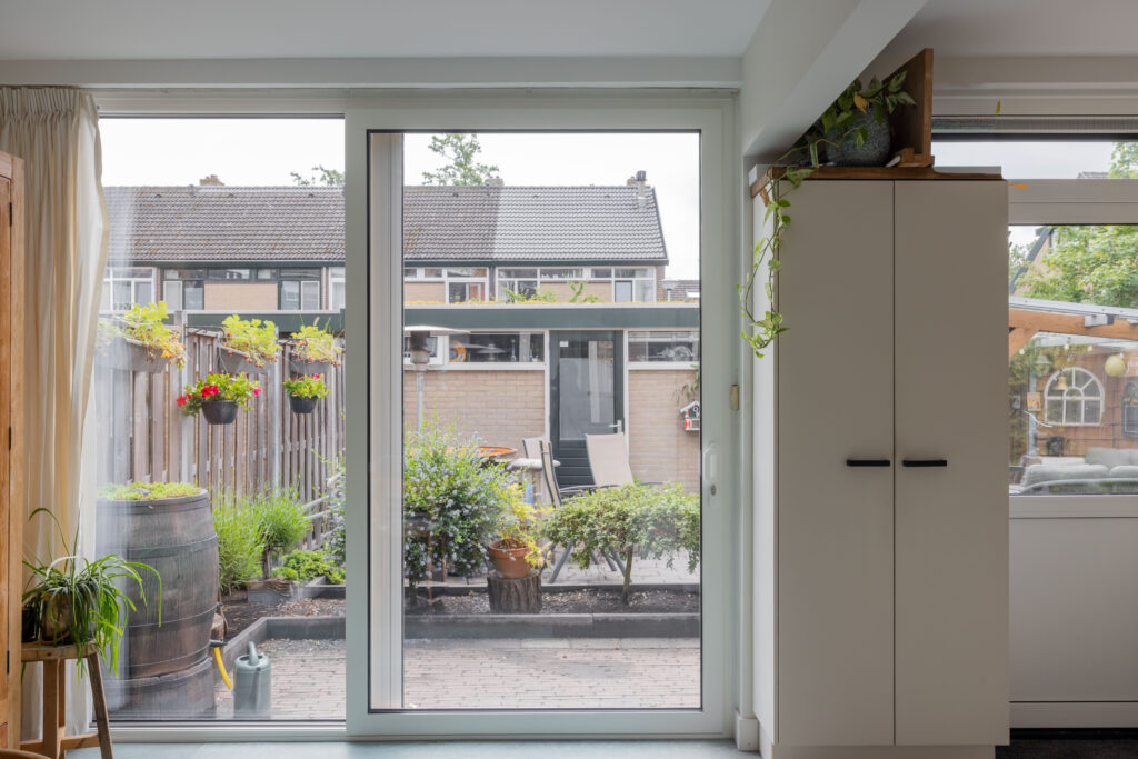 Moderne, grote schuifpui van Gewoon DICK gemonteerd in een keuken met direct zicht op een gezellige achtertuin.